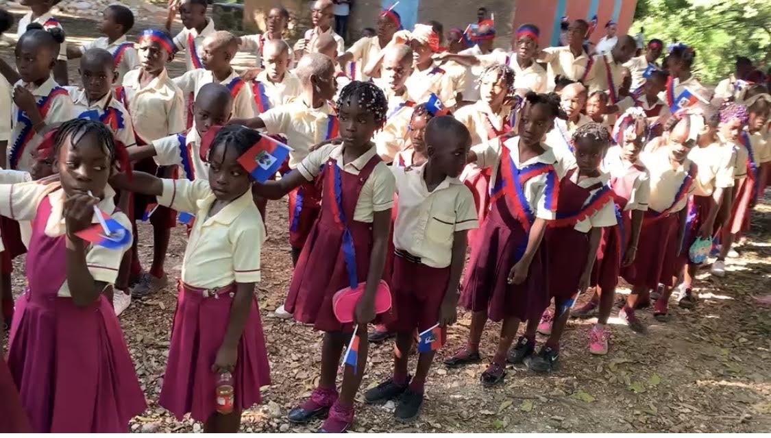 Children gathered outdoors with Haitian flags